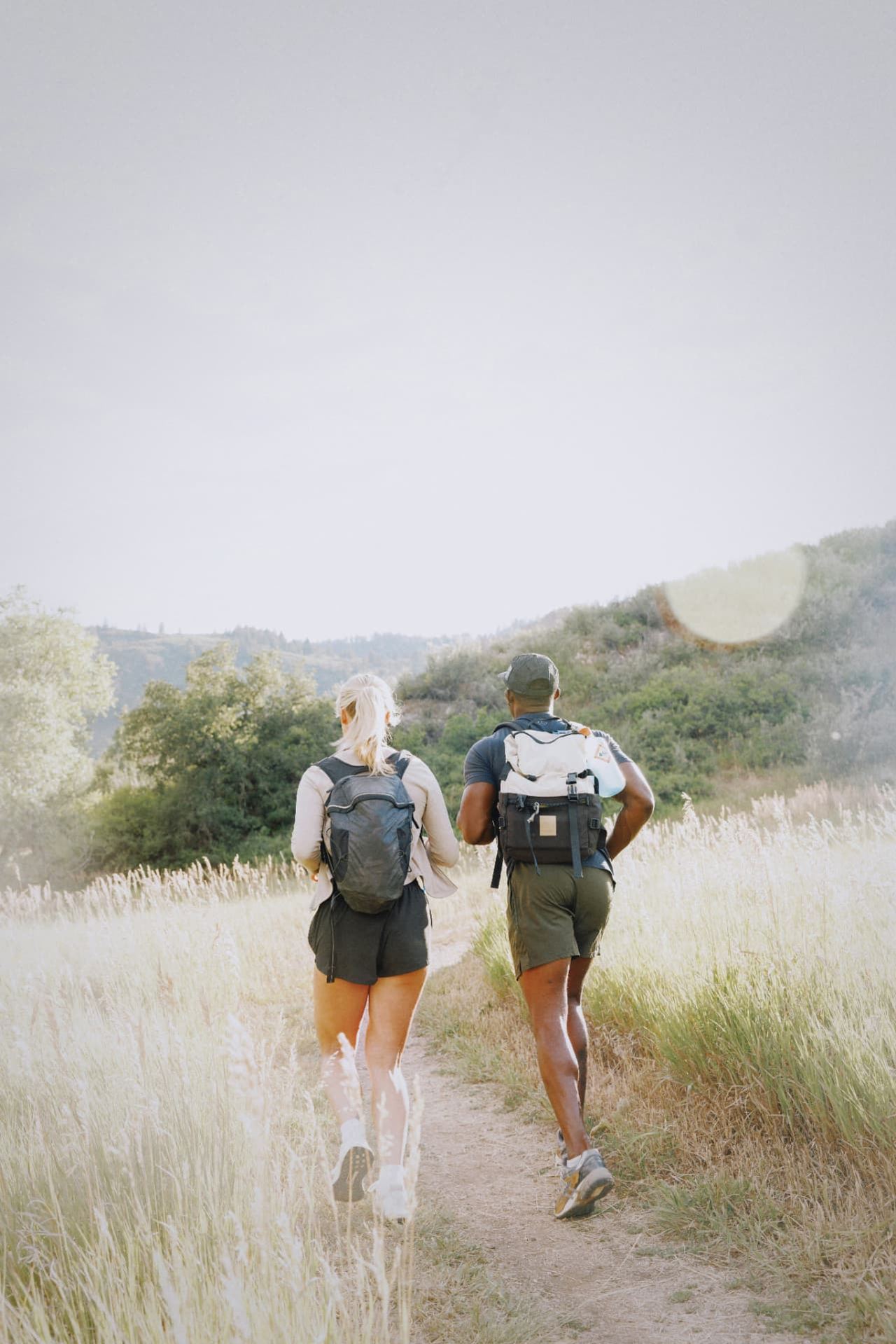 A couple with backpacks jogging along a golden grass trail toward the hills
