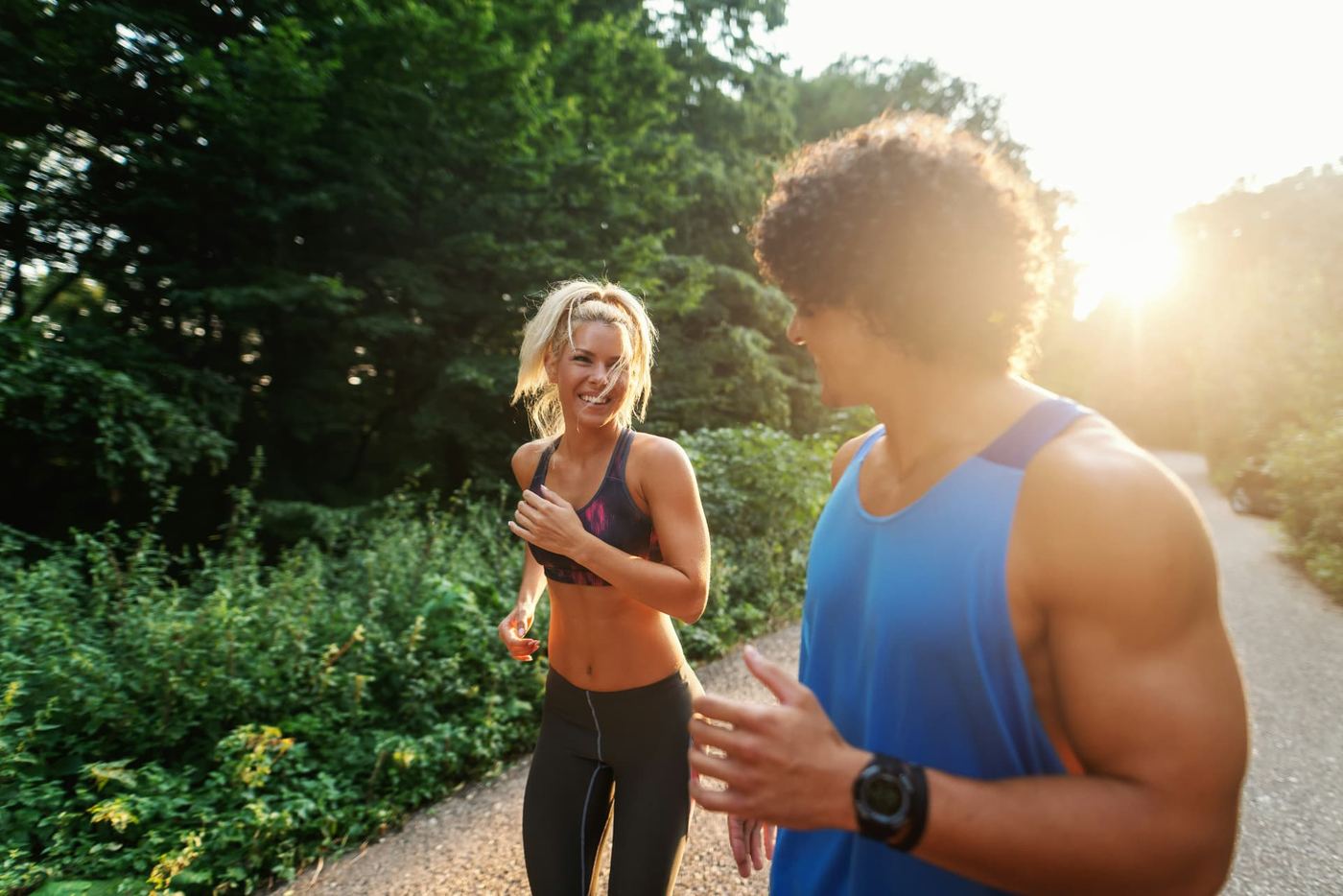 A couple running together, smiling, on a sunlit wooded path